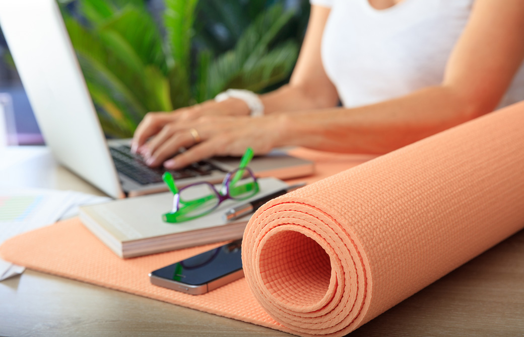 パソコンに向かって作業している人とヨガマット