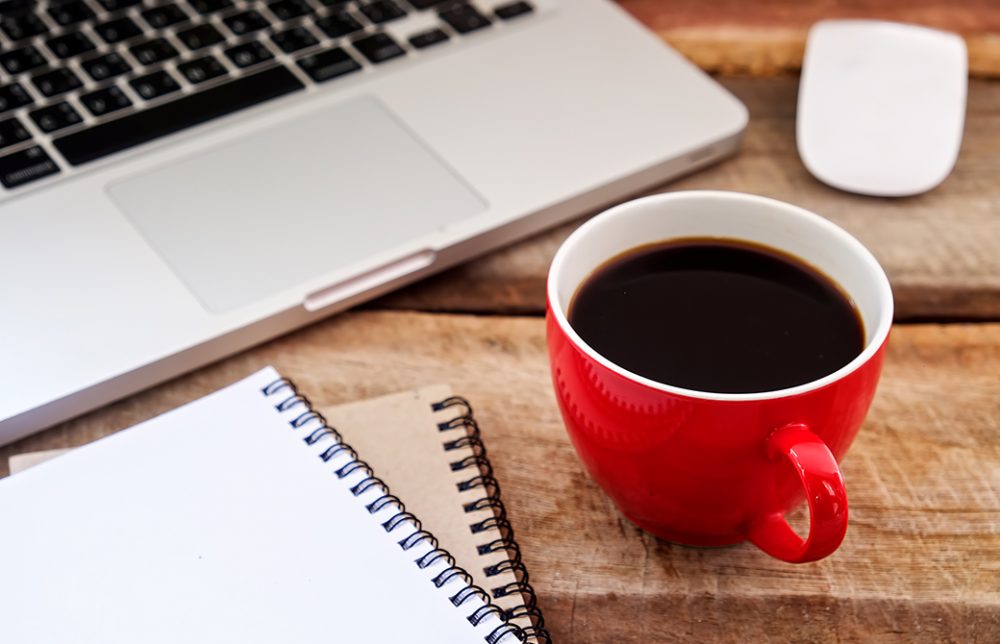 PCとコーヒーとノートが机の上にある写真