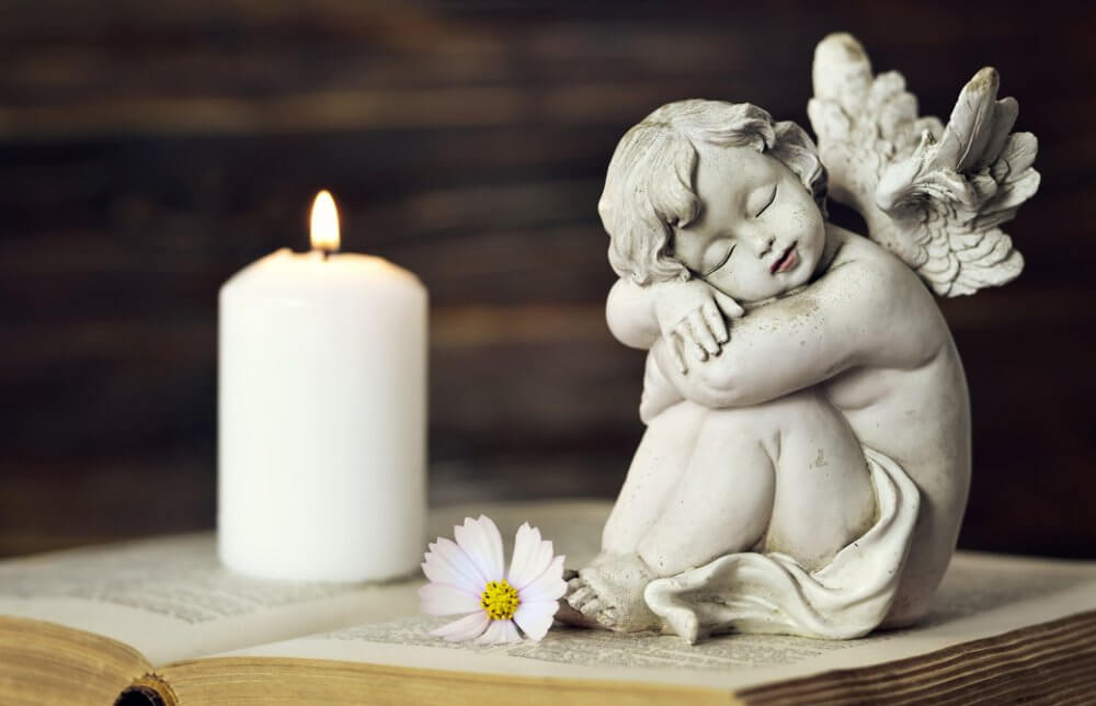 開かれた本の上に天使の置物とキャンドルが灯っている