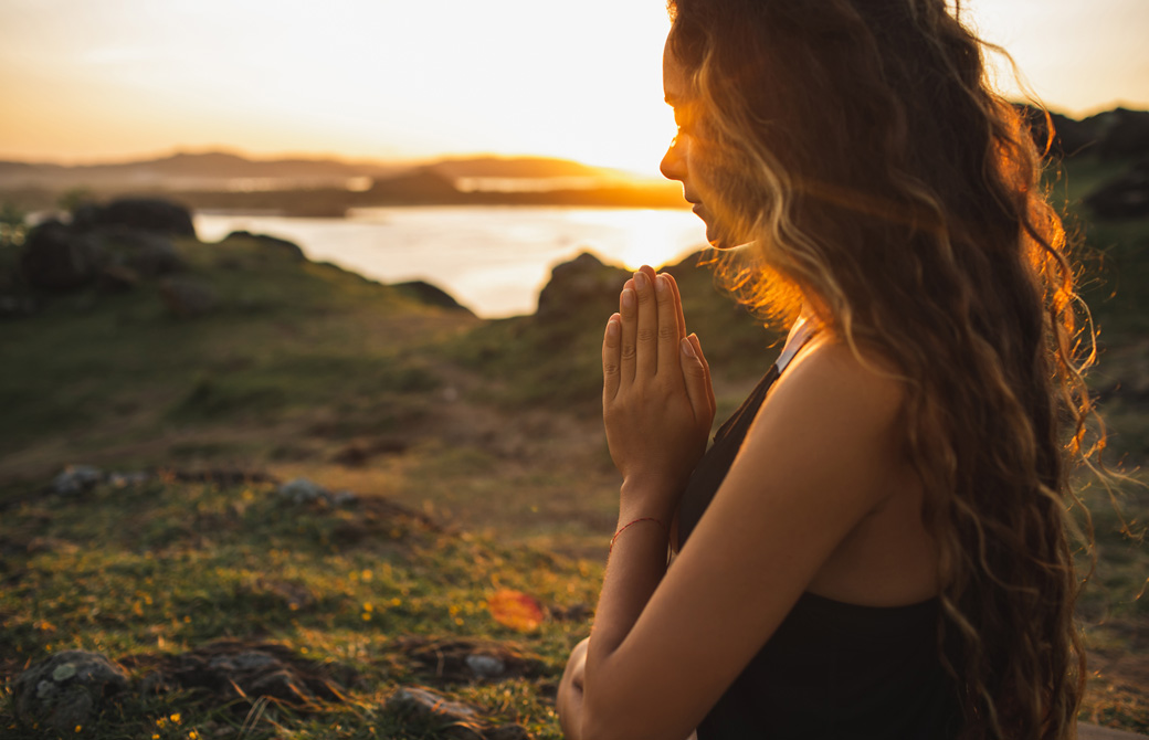 自然の中で手を合わせて祈る女性の横顔