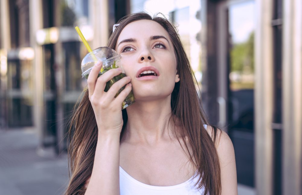 女性がドリンクカップを頬に当てて暑さを凌いでいる様子