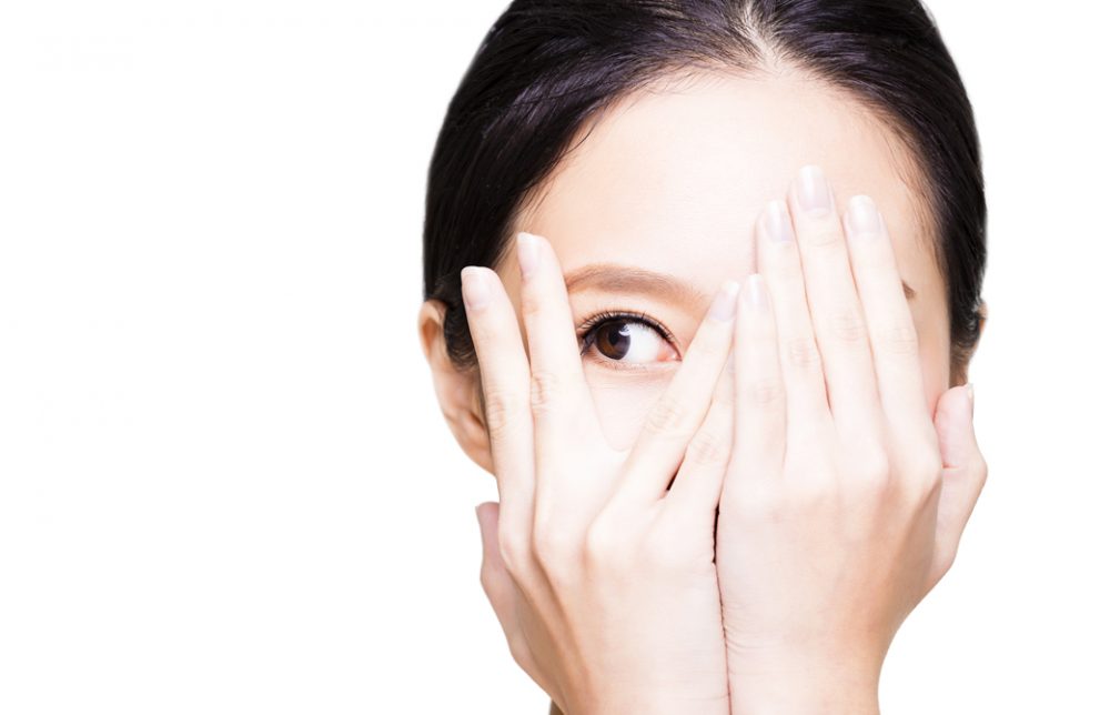 両手で顔を覆い右目だけのぞかせて横を見ている女性