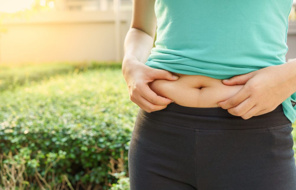 女性がお腹の肉をつまんでいるところ