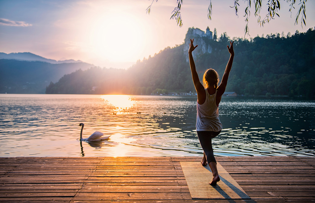 湖のほとりでヨガアサナをする女性と湖面を泳ぐ白鳥