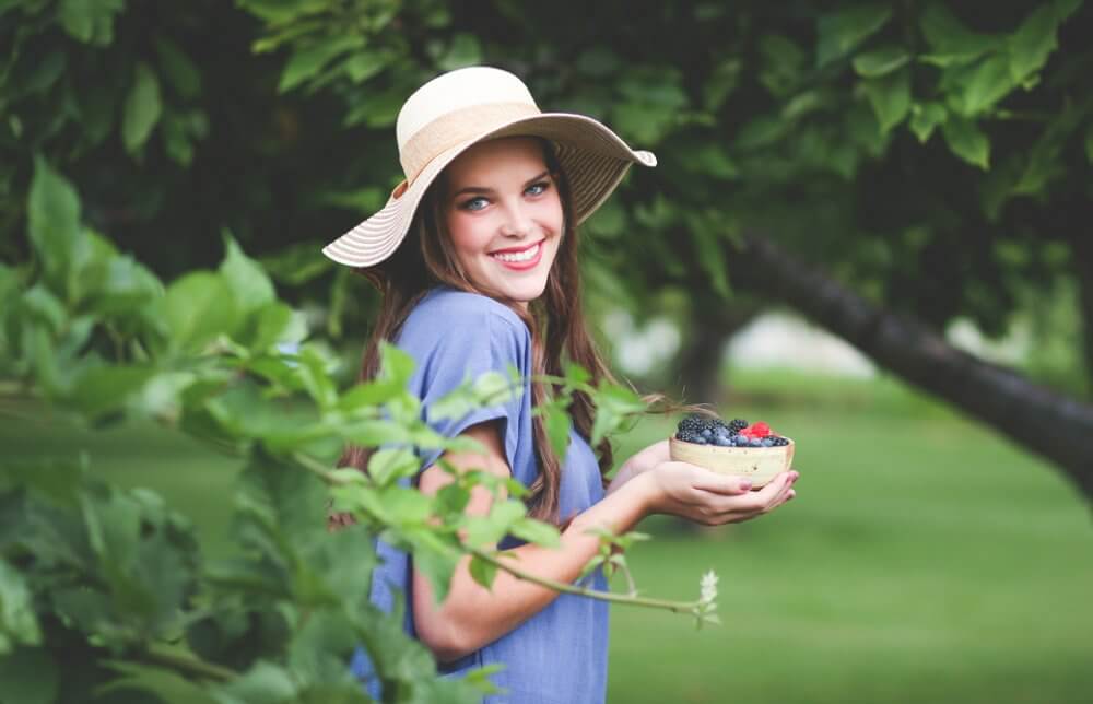木々に囲まれブルーベリーの入った器を持って微笑む女性