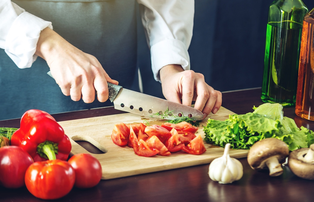 木製まな板の上でトマトやブロッコリーを切っている女性の手元