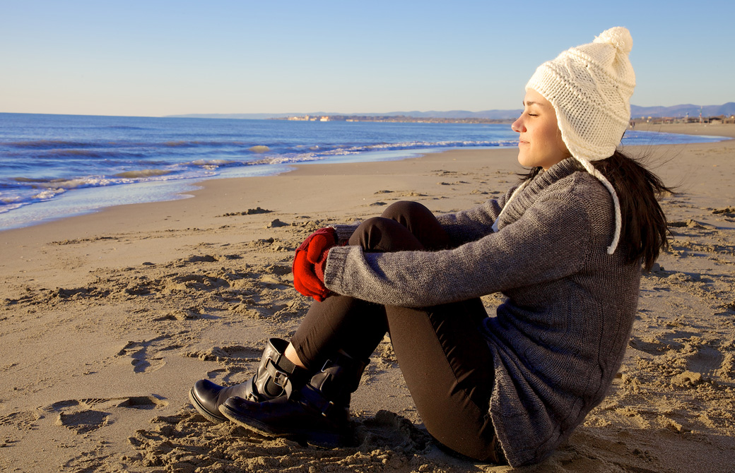 冬の海岸で日を浴びている女性
