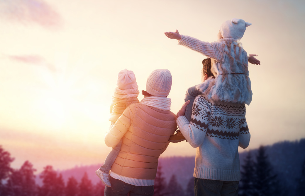 太陽に向かって腕を広げいてる少女を肩車する父親と横で赤ん坊を抱っこしている母親