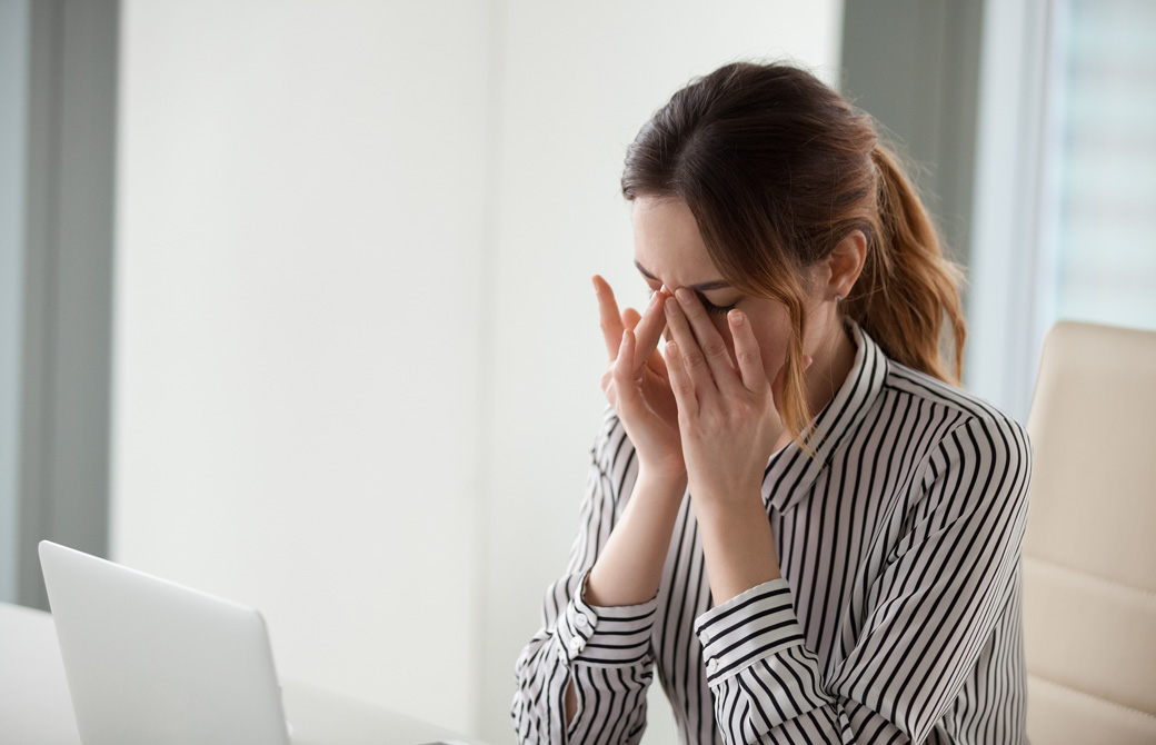 オフィスのデスくでドライアイを気にして両手で顔を覆う女性