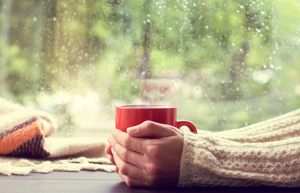 温かい飲み物の入ったカップを両手で包み込む人