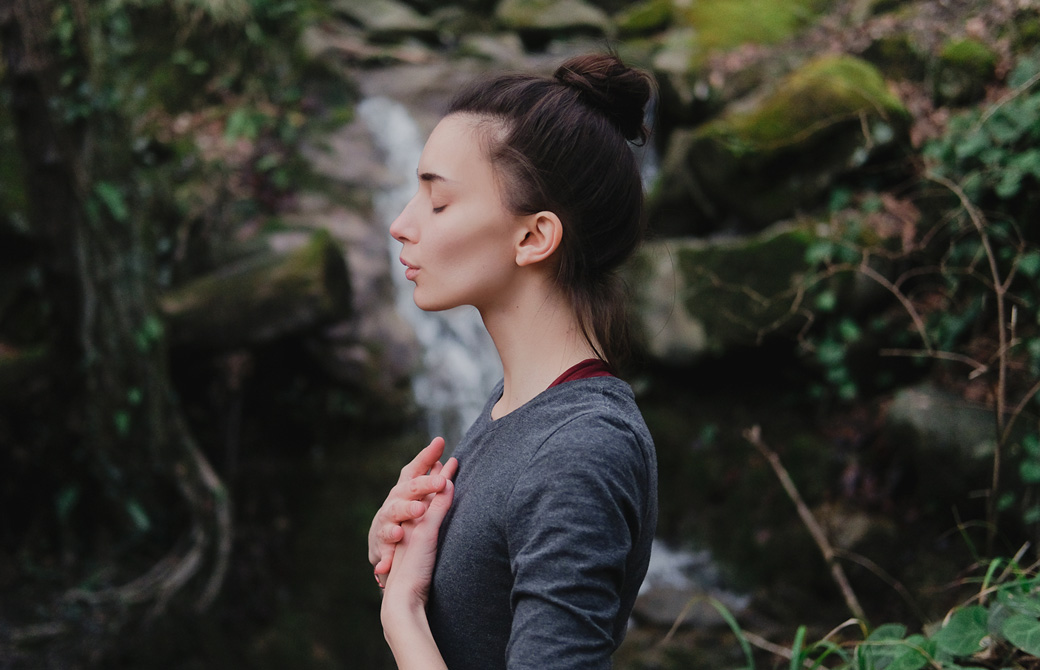 滝の前で両手を胸に当て目を閉じている女性の横姿
