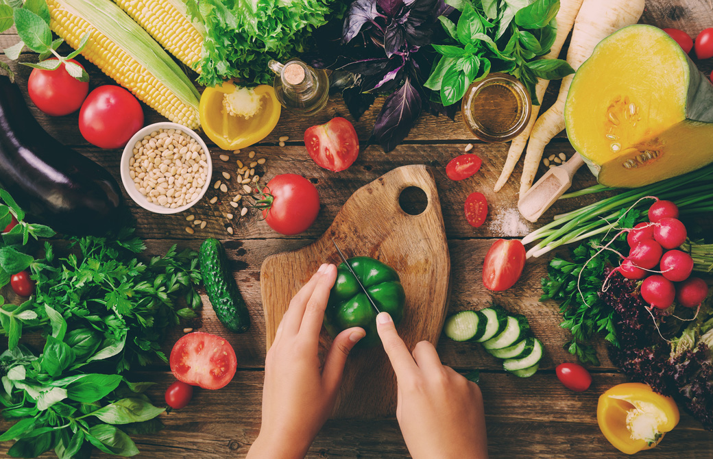 新鮮でカラフルな野菜たちとピーマンを切ろうとしている女性の手