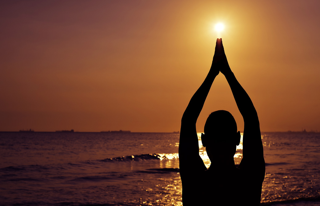 夕日に向かって腕を伸ばして手を合わせる女性のシルエット