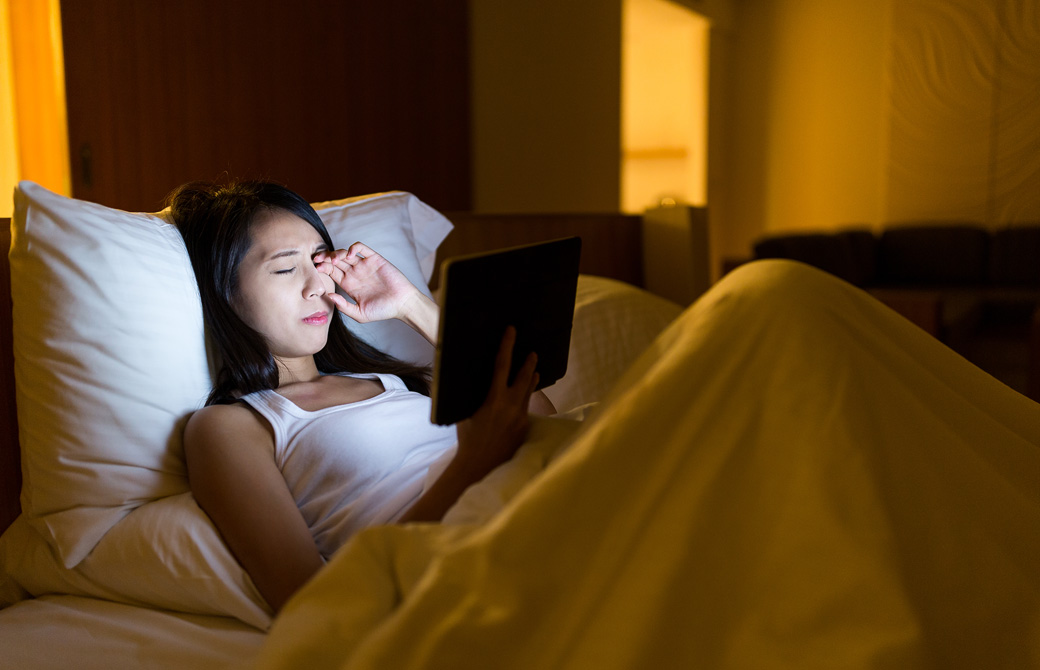 ベッドの上で夜更かししてタブレットを見ながら目をこすっている女性