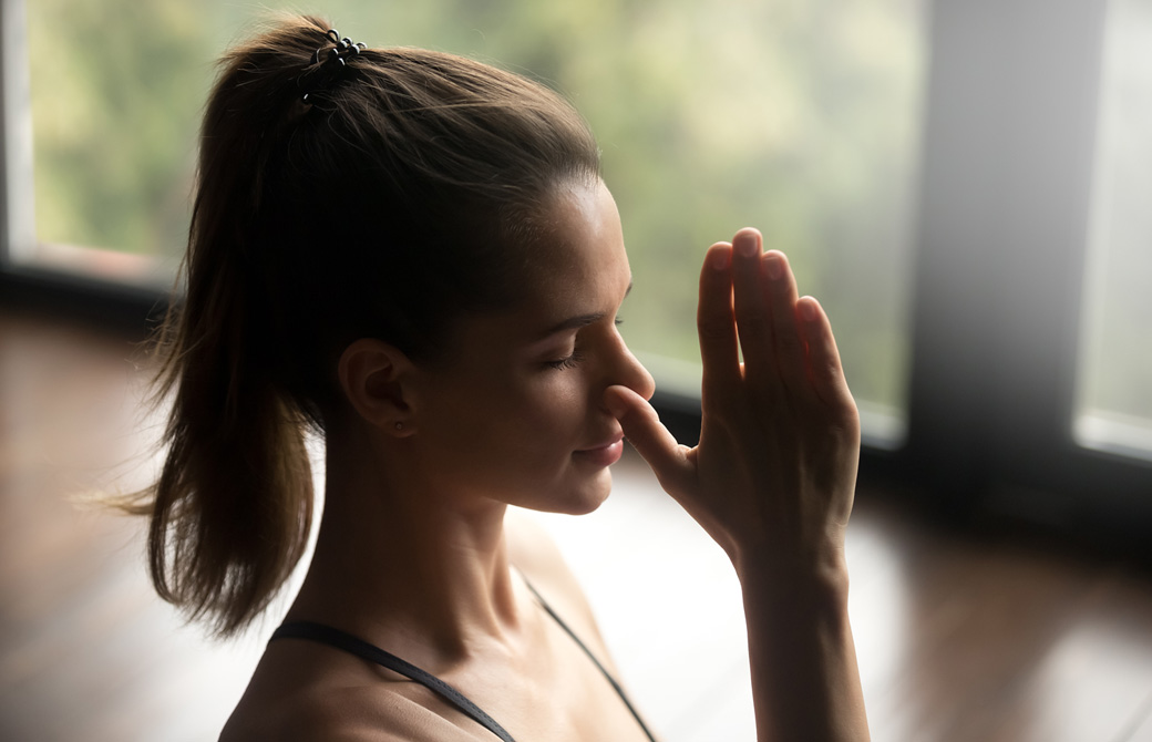 右の鼻腔を親指でおさえて左鼻だけで呼吸をしているポニーテールの女性