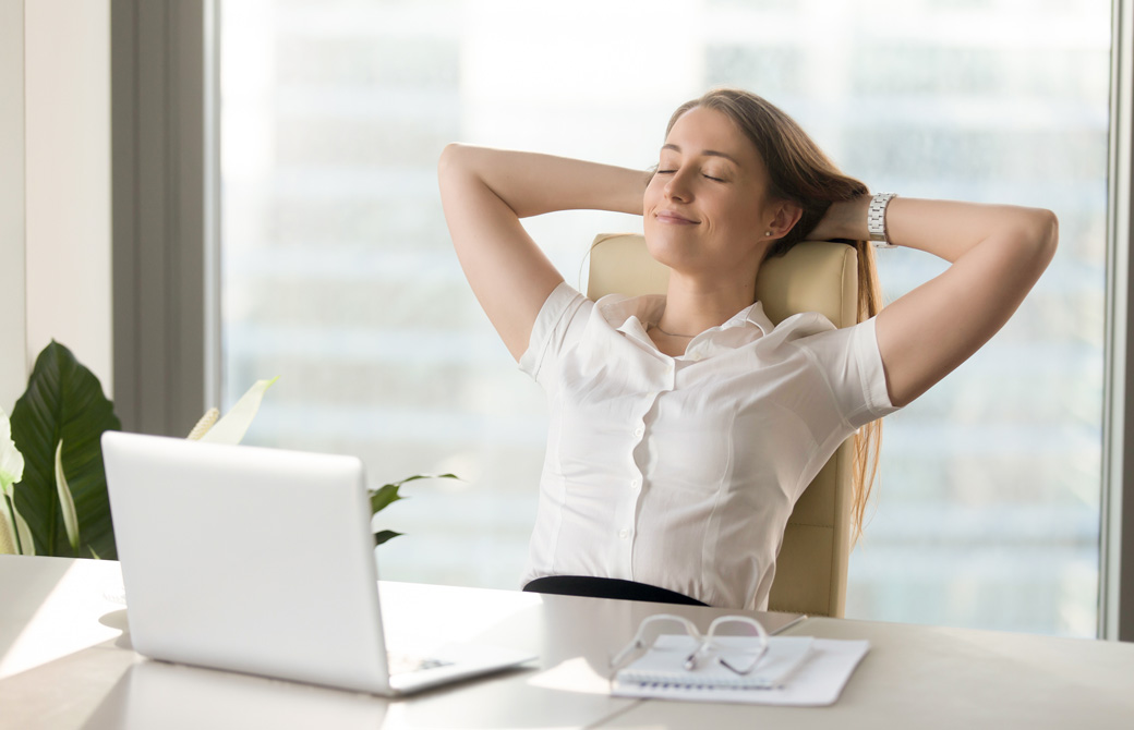 オフィスのデスクで頭の後ろに手を当ててリラックスしている女性
