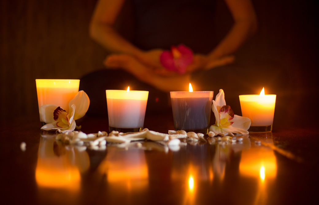 暗い室内の床にキャンドルがゆらゆら灯っていうるのをあぐらの女性が眺めている下半身だけ