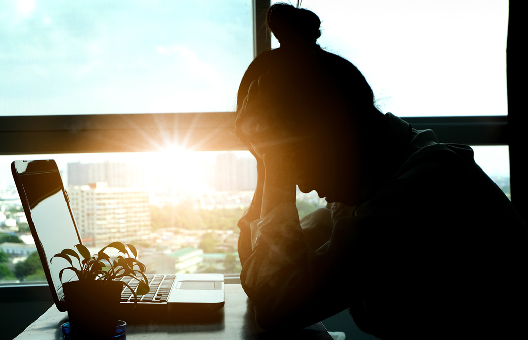 窓際のデスクでPCを前に頭をかかえてうつむいている女性