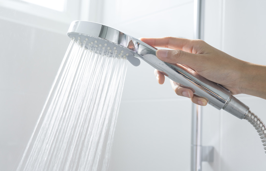 水が出ているシャワーヘッドを持つ手