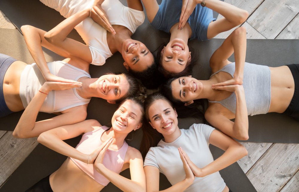 マットの上に輪になって横になり胸で合掌して笑顔の5人の女性たち