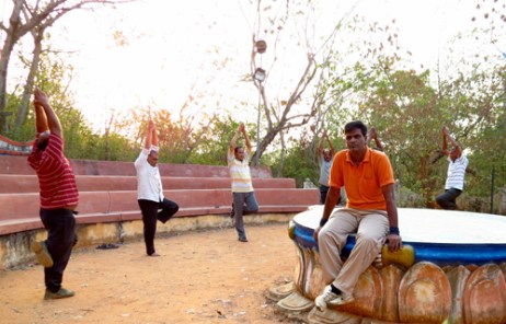 公園でヨガをしている人たちとこちらを見ているインド人男性