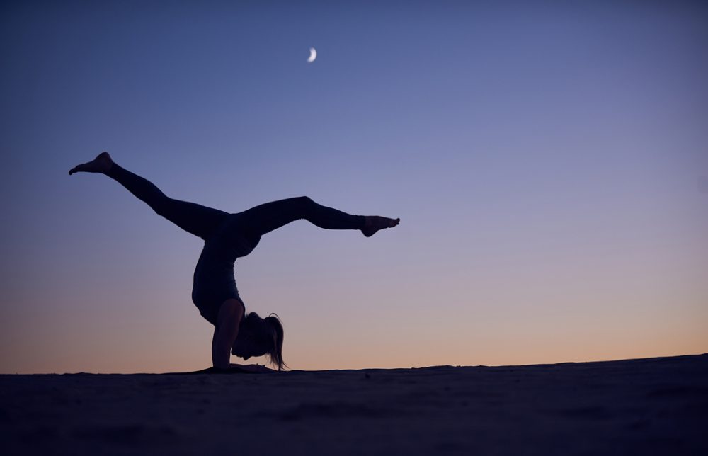 夕暮れ時に月明かりのもと逆転のポーズをとる女性