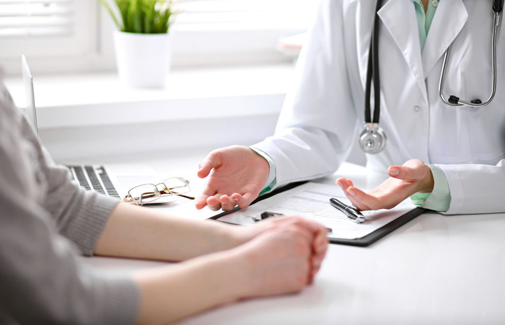 明るい部屋で向き合って座る医師と女性の腕の部分だけ