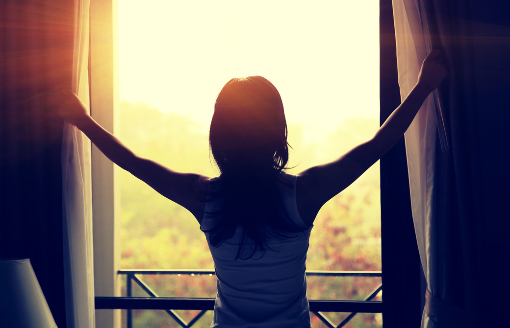 カーテンを両手で明けて外を眺める女性の後ろ姿