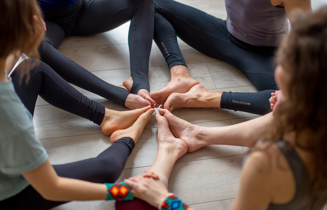 足の裏をつけて座った人たちが輪になってつま先を繋げて手を握っている