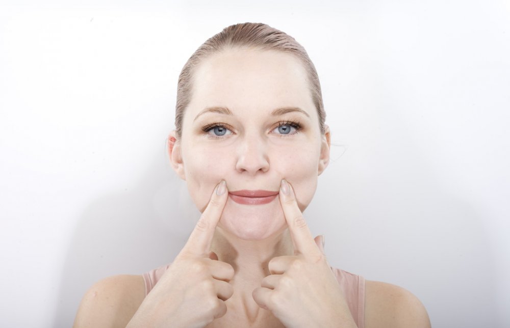 口角を指で引き上げ顔ヨガをしている女性