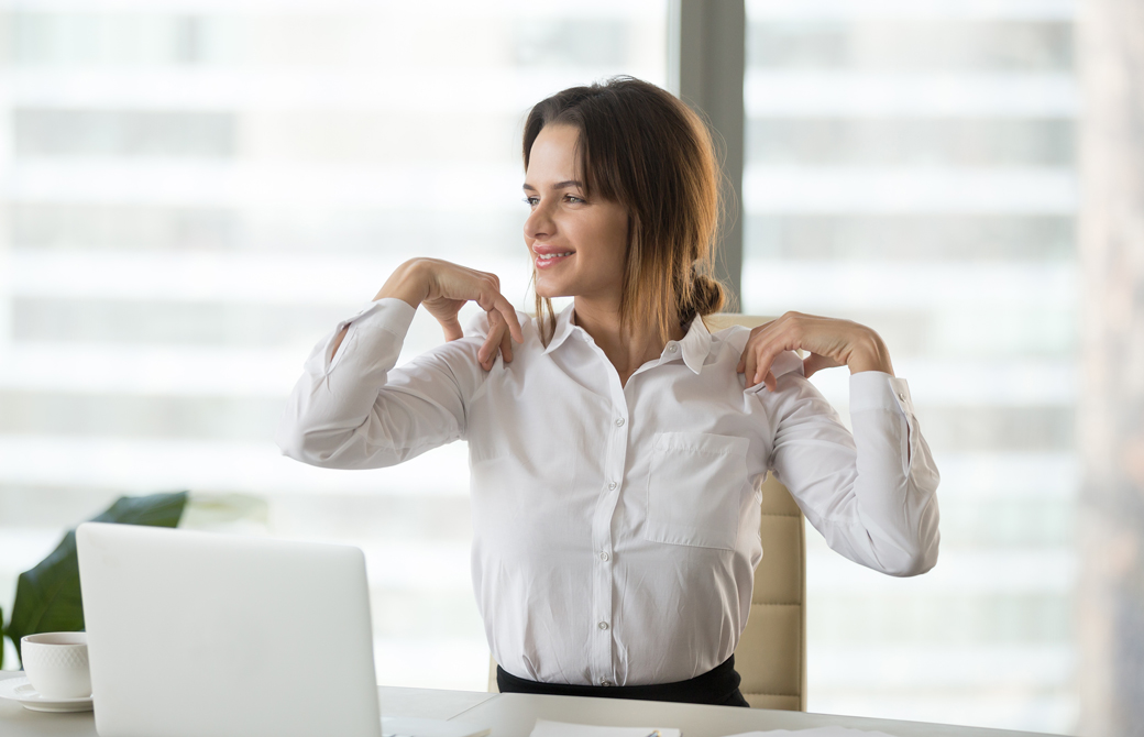 オフィスデスクに座りながら両肩を回して微笑んでいる女性