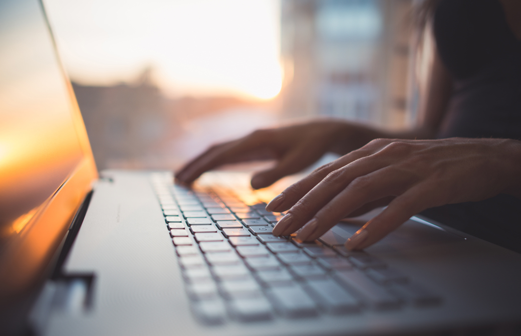夕陽に照らされたオフィスにあるラップトップとタイピングしている女性の手
