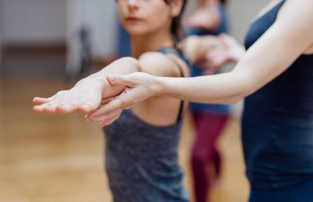 戦士のポーズ2番の腕をアジャストしているヨガインストラクター