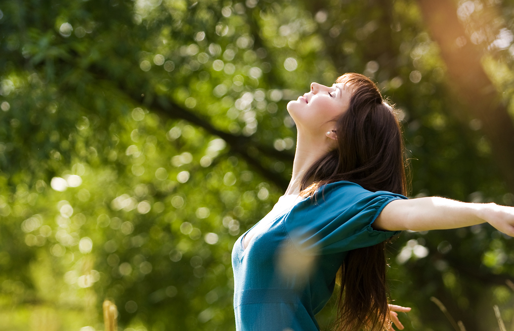 森林の中で女性が空をあおいで気持ち良さそうに両腕を開いている