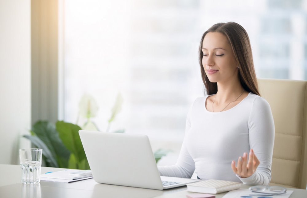 デスクでPCを前に目を閉じ瞑想をしている女性