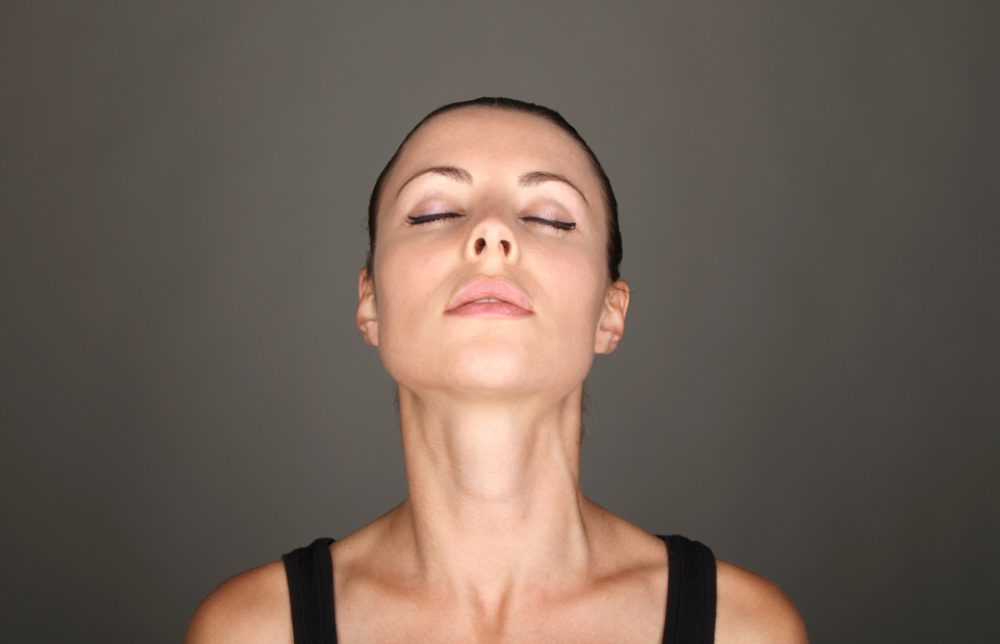女性が目を閉じてあごを突き出し首元のストレッチをしている