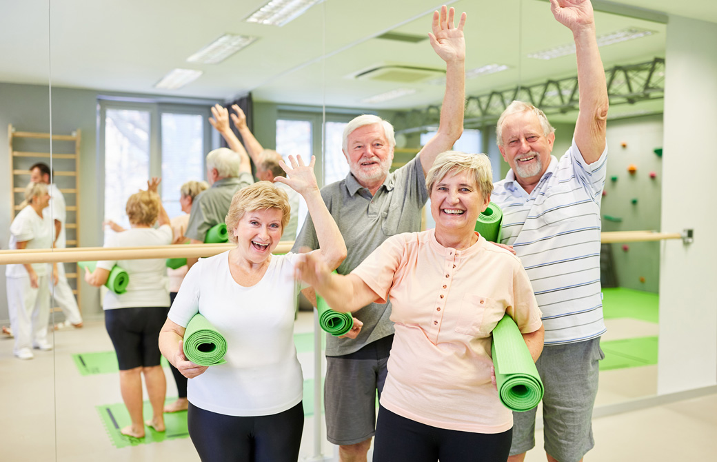 ヨガマットを持って笑顔で手をあげる老人たち