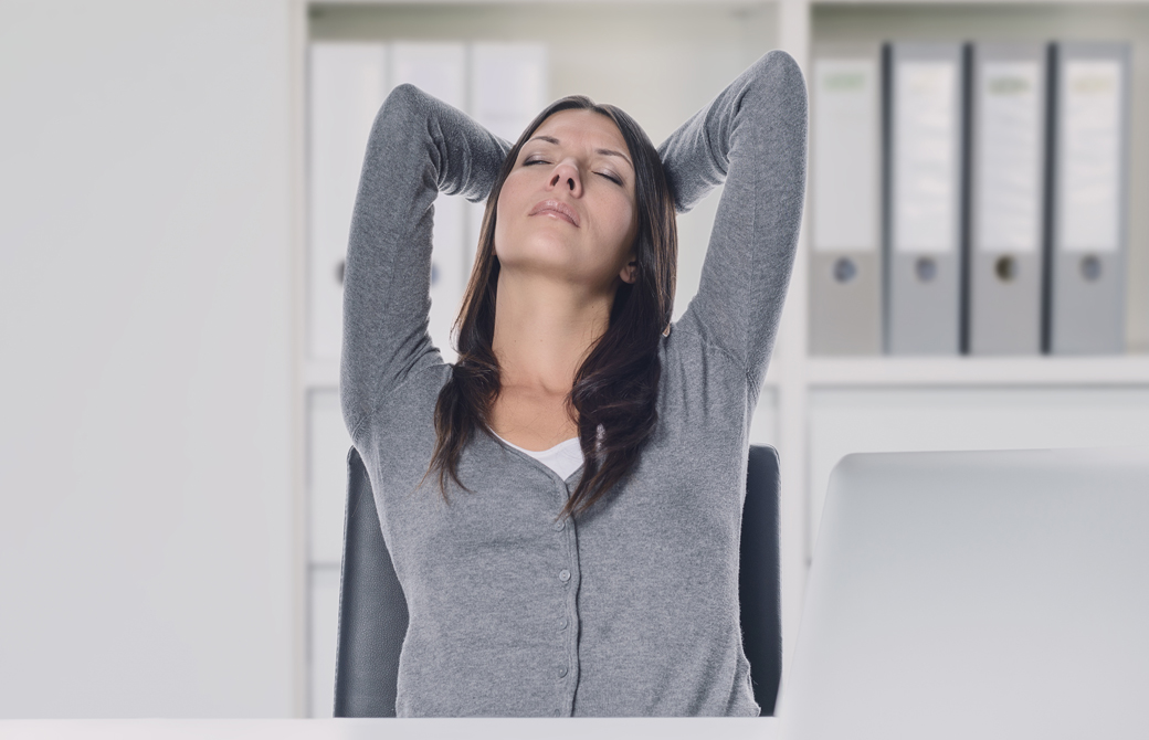 女性がデスクで座りながら後頭部をおさえてストレッチしている