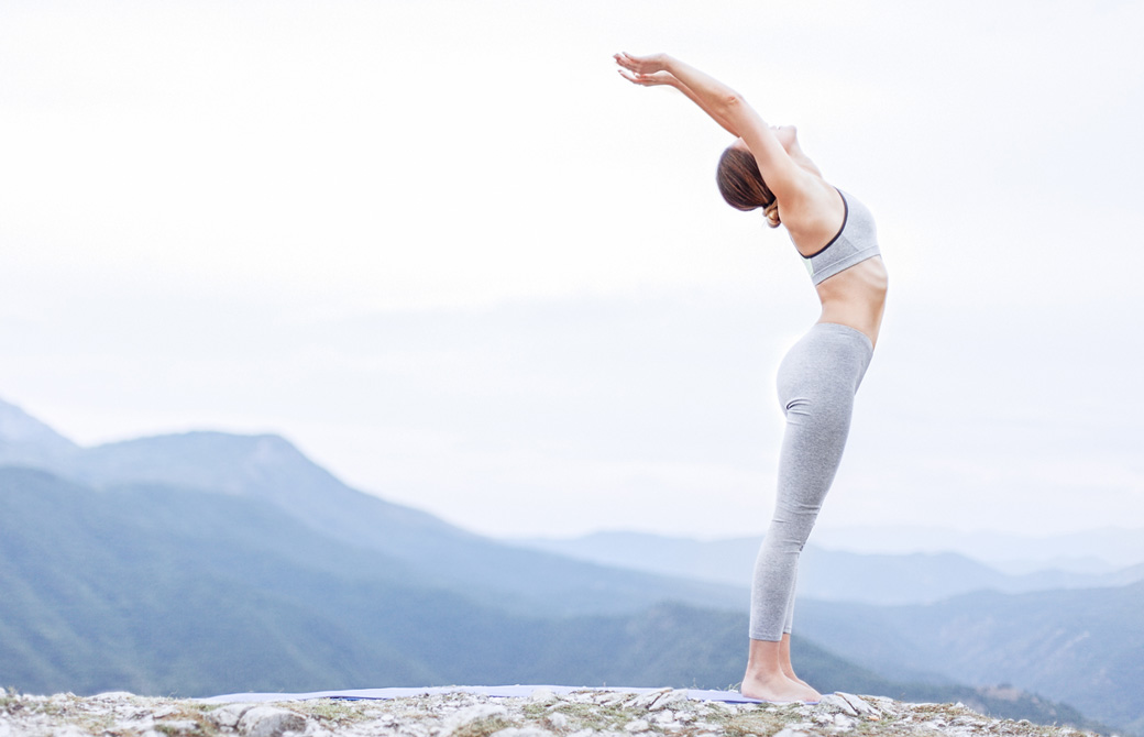 山を臨む屋外で心地よく腕を伸ばし立位の後屈をする女性