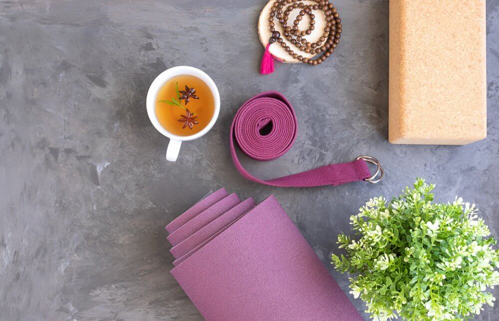 丸めたヨガマットとハーブティーのカップ、ヨガベルトとブロックなどが置かれている