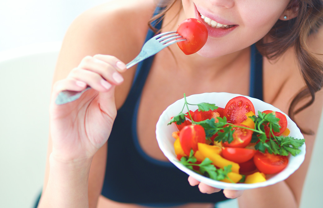 カラフルなサラダボールを美味しそうに食べる女性