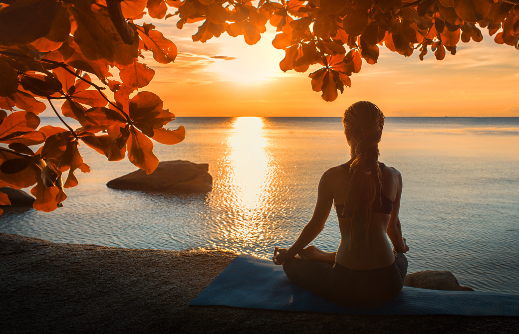 海辺でサンセットを受けて瞑想をする女性