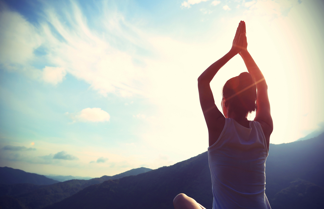 あぐらで頭の上で手を合わせ空に向って背筋を伸ばしている女性