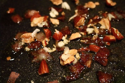 オイルをひいたフライパンでベーコンとアーモンドを炒めている