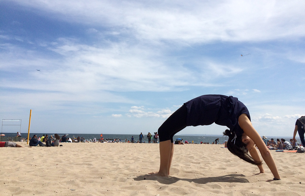 MahokoがNYのビーチで車輪のポーズをとっている