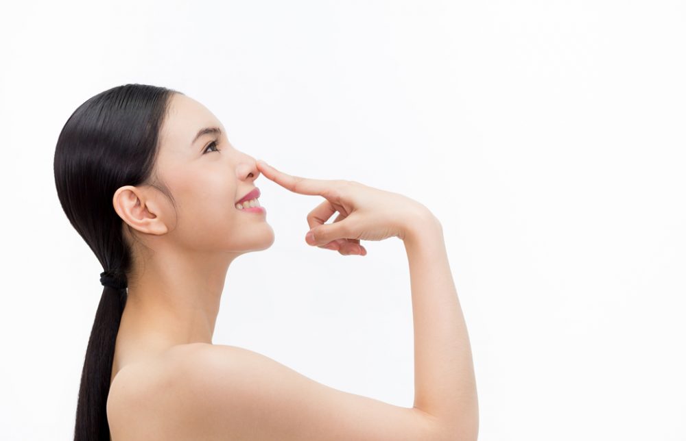 鼻を人差し指で指して微笑む女性の横姿