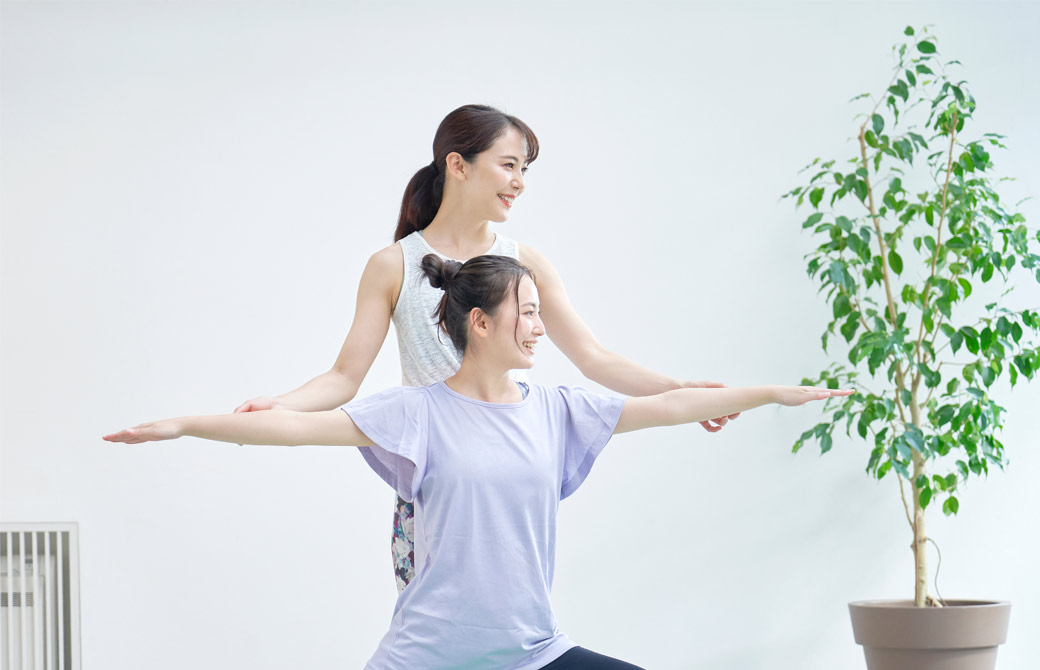 女性のヨガインストラクターが、女性の生徒さんの手を掴んでポーズを支えている