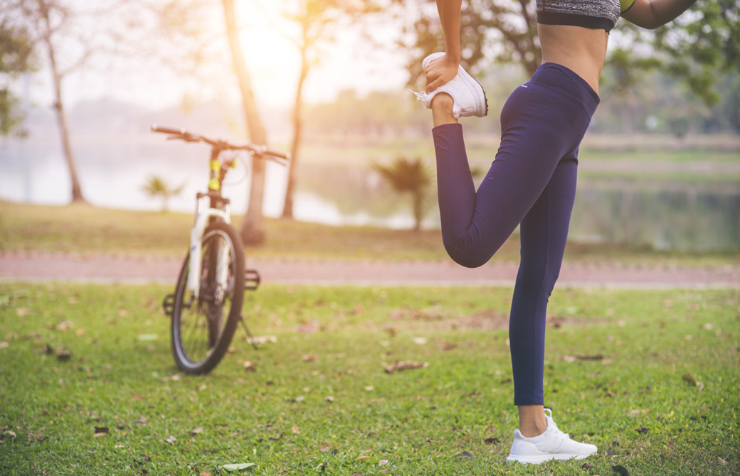 公園の芝生の上で片脚を持ちストレッチする女性と自転車
