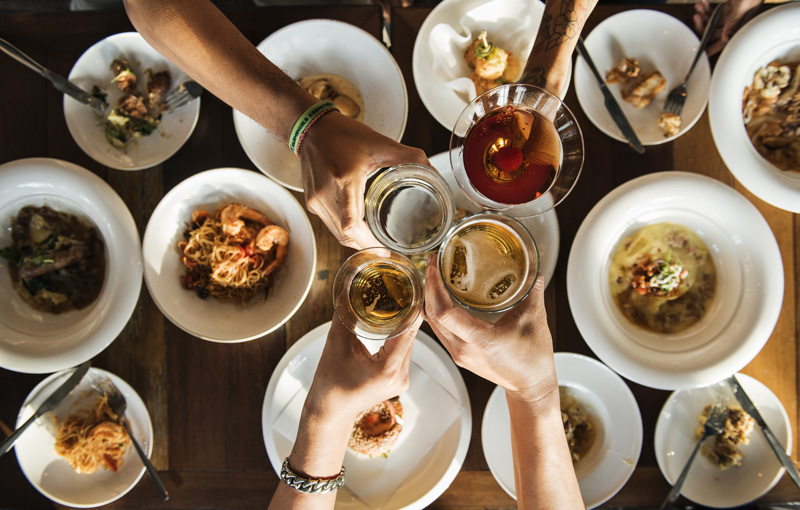 様々な料理の上で4人の手が乾杯している