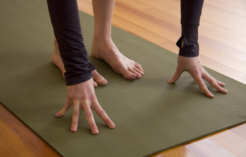 ヨガマットに前屈で手をついている女性